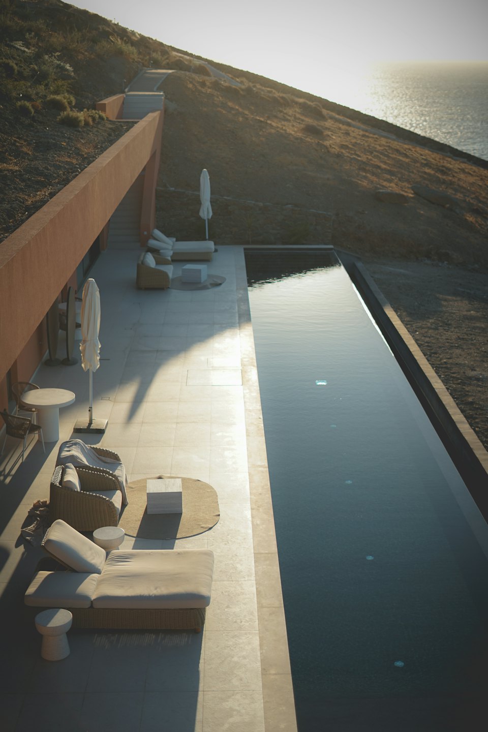 Infinity pool and patio furniture overlooking the ocean from a hillside.