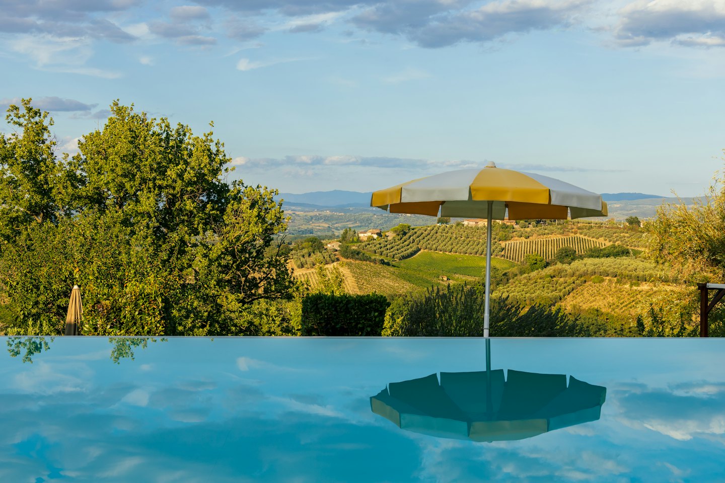 Yellow and white striped umbrella reflected in an infinity pool.