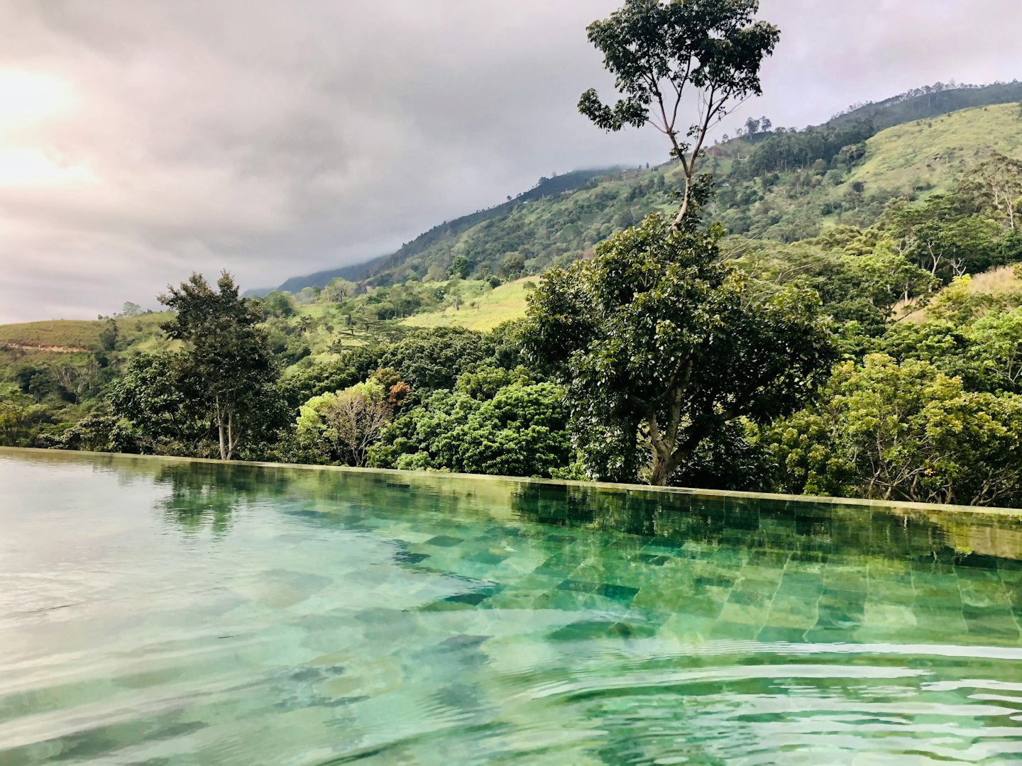 Turquoise infinity pool overlooking rolling green forested hills.