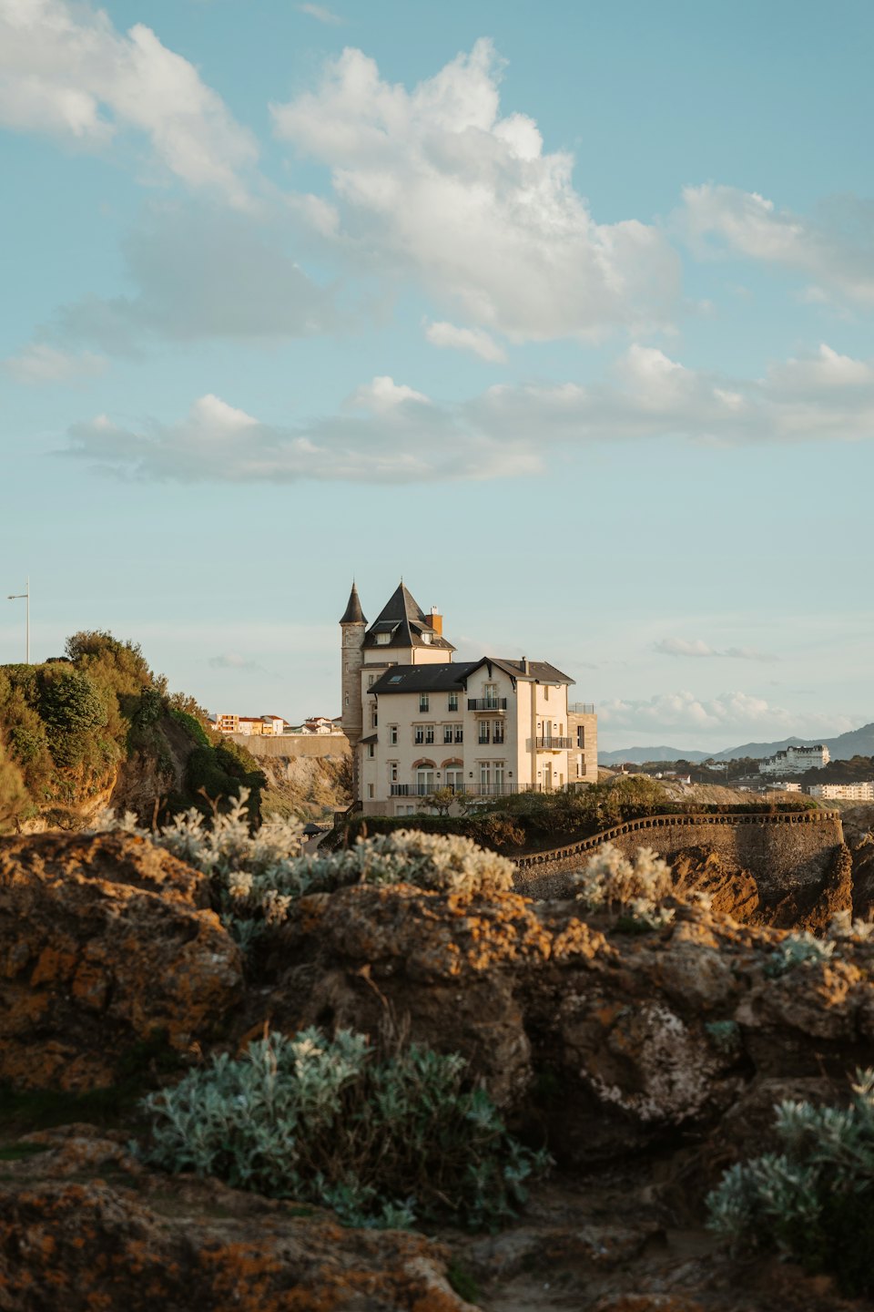Cream villa with turret on cliff edge at sunset.